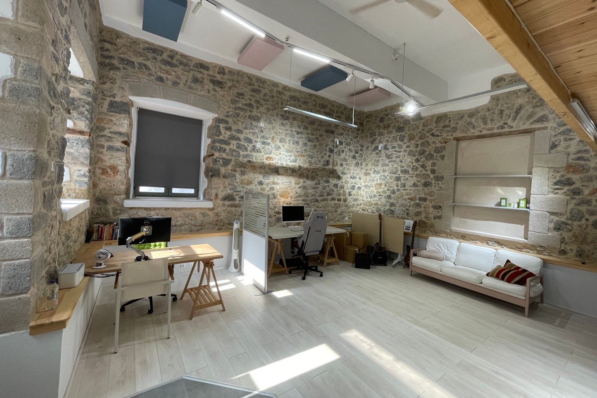 The animate room: stone walls, desks, a white sofa and sunlight on a pale wooden floor